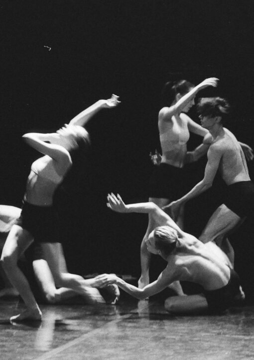 Artistic black and white photo of a group of ballet dancers in motion on stage.