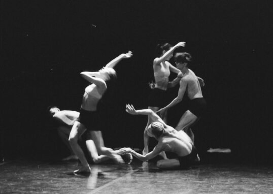 Artistic black and white photo of a group of ballet dancers in motion on stage.