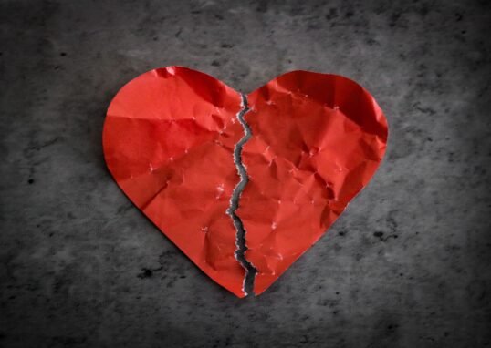 A torn red paper heart symbolizing heartbreak and lost romance.