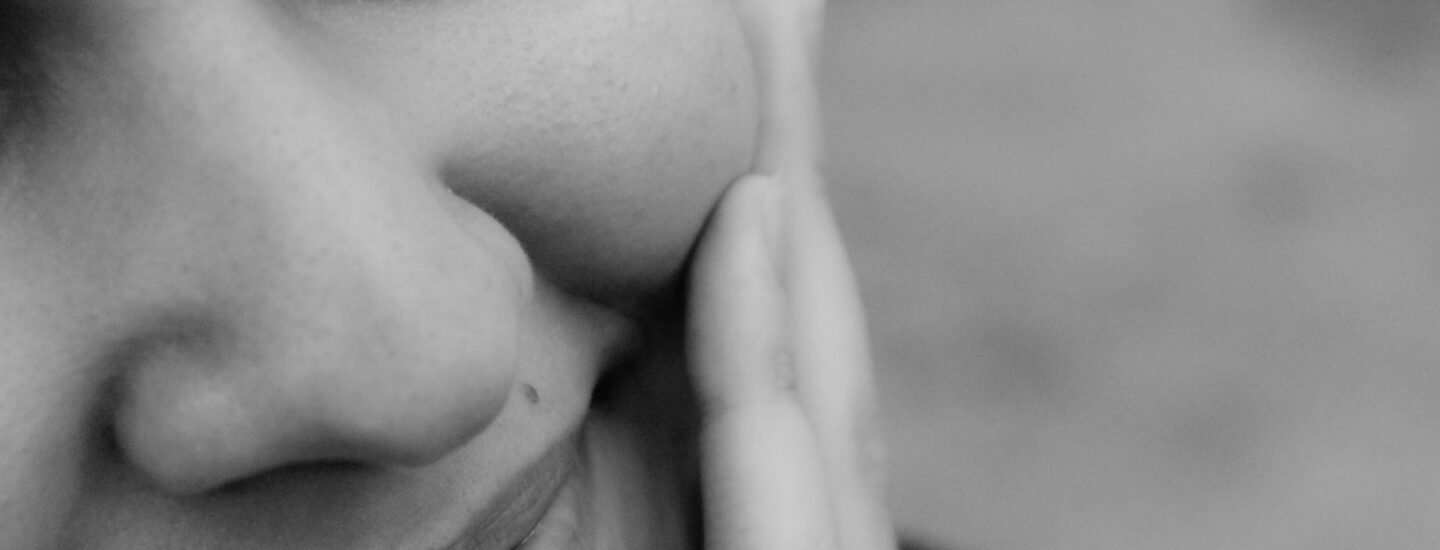 Close-up black and white photo of a smiling woman with hand on cheek.