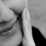 Close-up black and white photo of a smiling woman with hand on cheek.