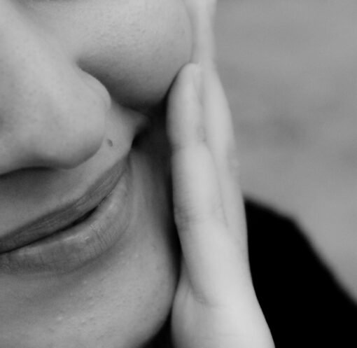 Close-up black and white photo of a smiling woman with hand on cheek.