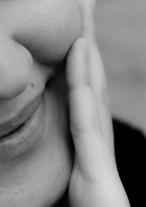 Close-up black and white photo of a smiling woman with hand on cheek.