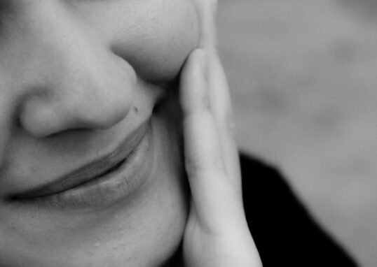 Close-up black and white photo of a smiling woman with hand on cheek.