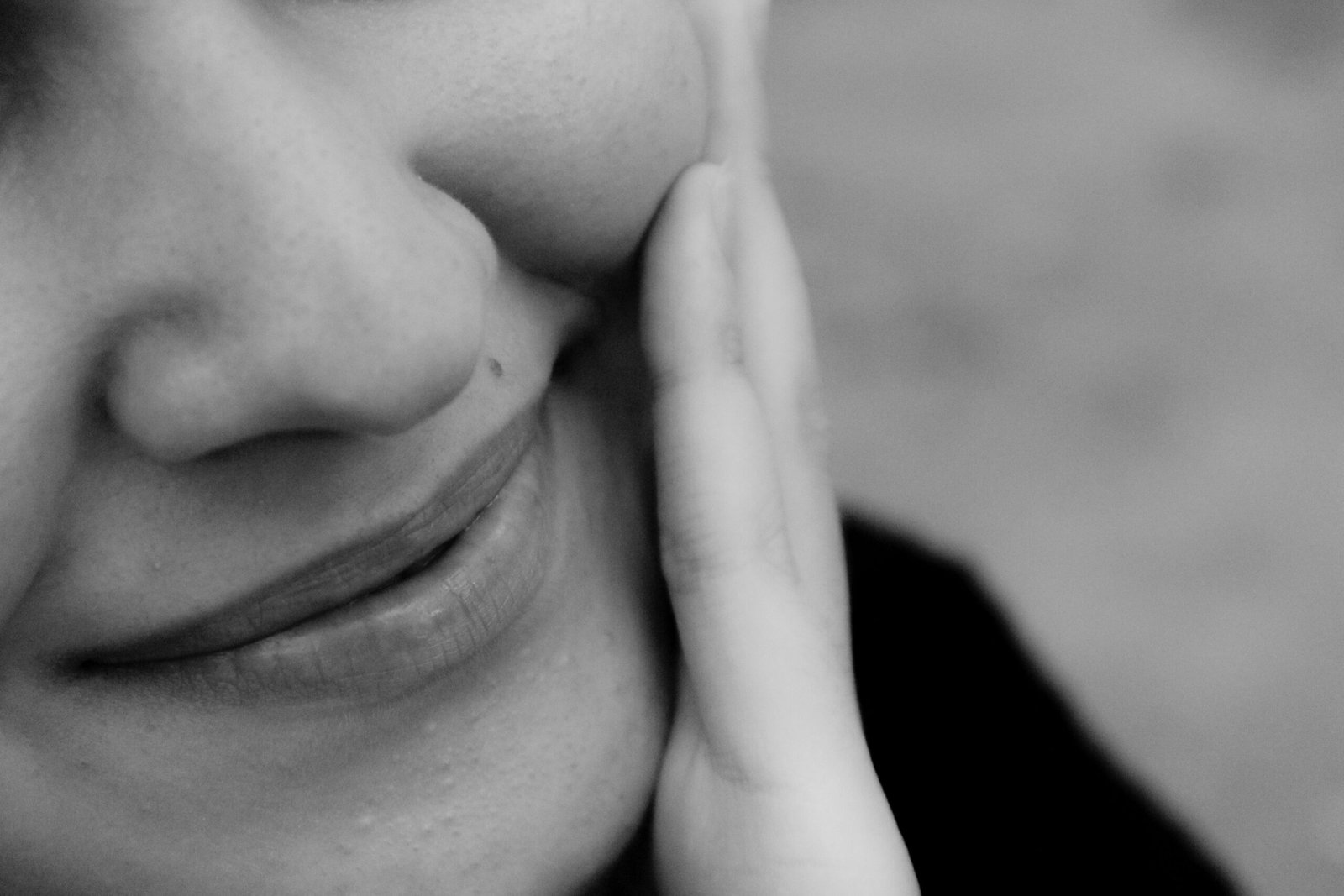 Close-up black and white photo of a smiling woman with hand on cheek.