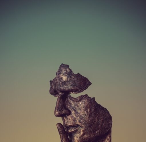 Bronze sculpture of a face missing parts and a finger to its lips, suggesting silence and mystery.