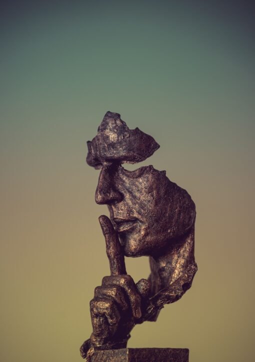 Bronze sculpture of a face missing parts and a finger to its lips, suggesting silence and mystery.