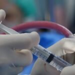 Surgeon's hands handling syringe during a medical procedure in a sterile operating room.