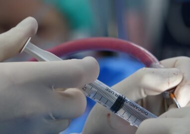 Surgeon's hands handling syringe during a medical procedure in a sterile operating room.