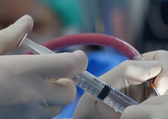 Surgeon's hands handling syringe during a medical procedure in a sterile operating room.