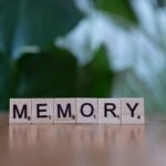Wooden letter tiles spelling 'Memory' on a wooden table with blurred green background.