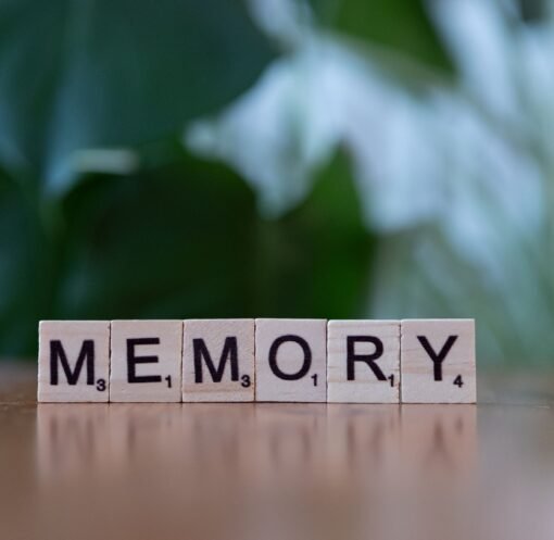 Wooden letter tiles spelling 'Memory' on a wooden table with blurred green background.