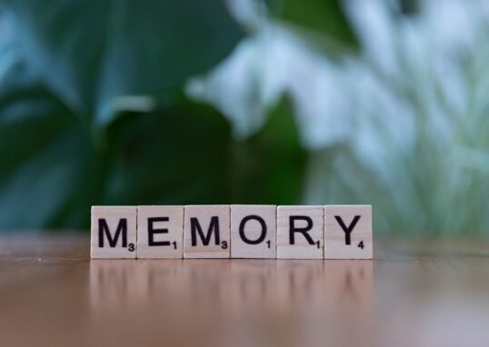 Wooden letter tiles spelling 'Memory' on a wooden table with blurred green background.