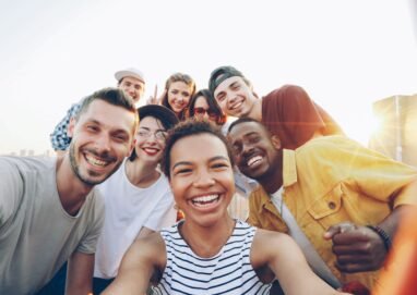 A diverse group of friends taking a joyful selfie outdoors during sunset.
