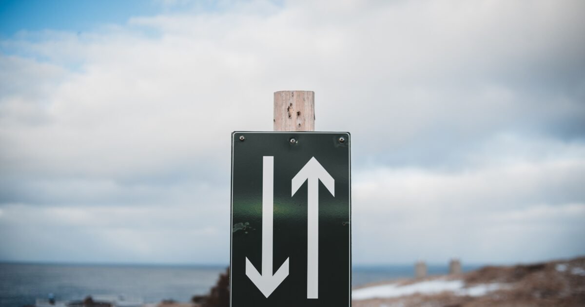 Sign of two way trail on sandy shore of calm sea with snow under cloudy sky on winter day