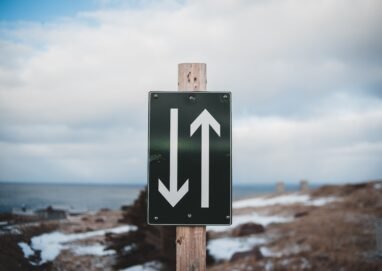 Sign of two way trail on sandy shore of calm sea with snow under cloudy sky on winter day