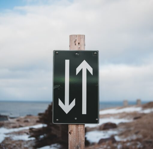 Sign of two way trail on sandy shore of calm sea with snow under cloudy sky on winter day