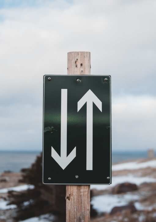 Sign of two way trail on sandy shore of calm sea with snow under cloudy sky on winter day