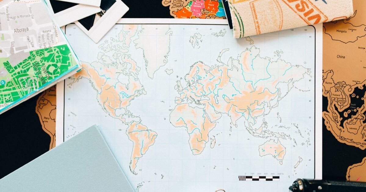 Flat lay of travel essentials including a world map, compass, and planner, perfect for planning your next adventure.