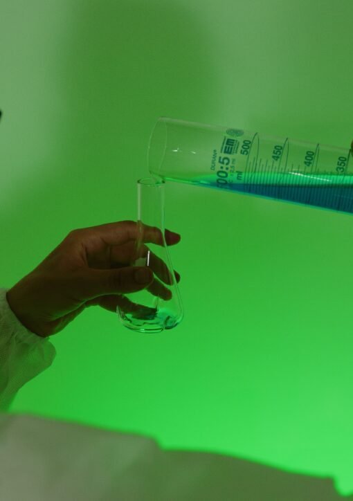 Scientist carefully pouring blue liquid into a test tube under green light.