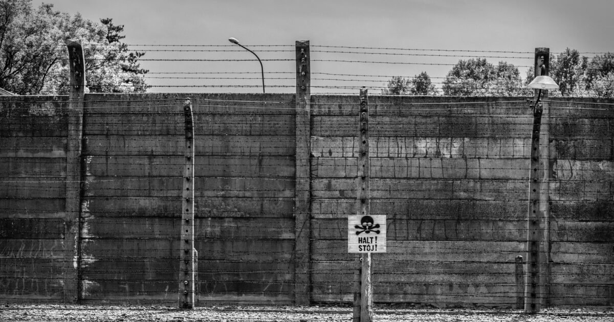 Monochrome image of Auschwitz Birkenau fence with warning sign in Poland.