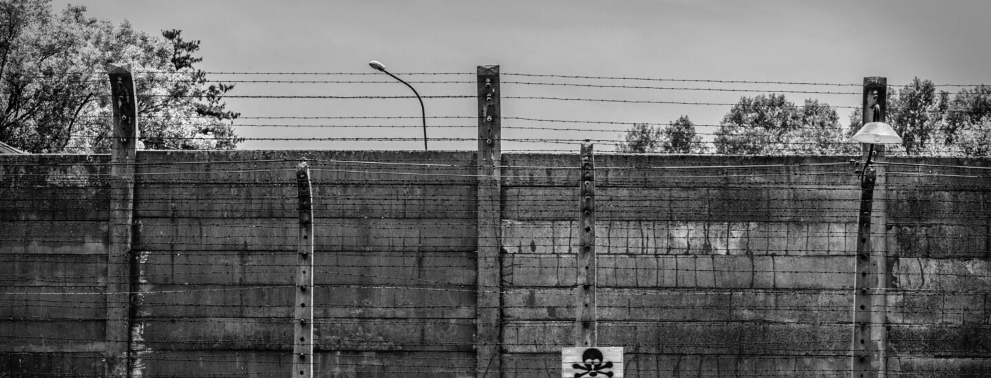 Monochrome image of Auschwitz Birkenau fence with warning sign in Poland.