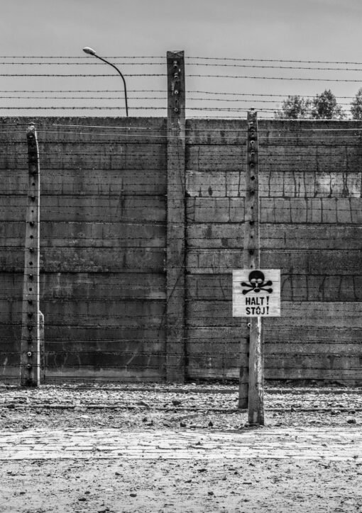 Monochrome image of Auschwitz Birkenau fence with warning sign in Poland.