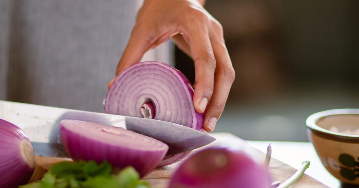 A close-up shot of a hand slicing a red onion on a wooden cutting board, showcasing freshness.