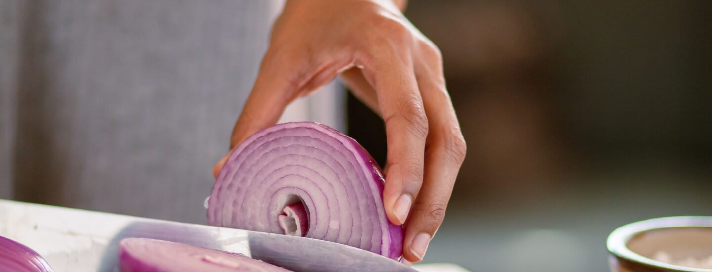A close-up shot of a hand slicing a red onion on a wooden cutting board, showcasing freshness.