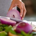 A close-up shot of a hand slicing a red onion on a wooden cutting board, showcasing freshness.