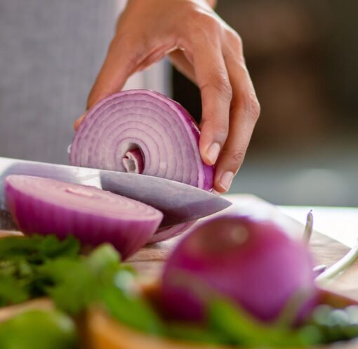 A close-up shot of a hand slicing a red onion on a wooden cutting board, showcasing freshness.