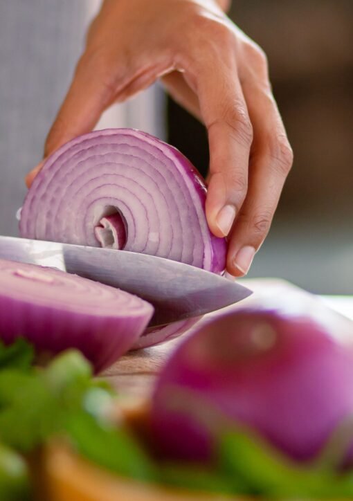 A close-up shot of a hand slicing a red onion on a wooden cutting board, showcasing freshness.