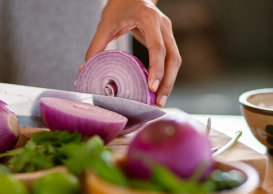 A close-up shot of a hand slicing a red onion on a wooden cutting board, showcasing freshness.