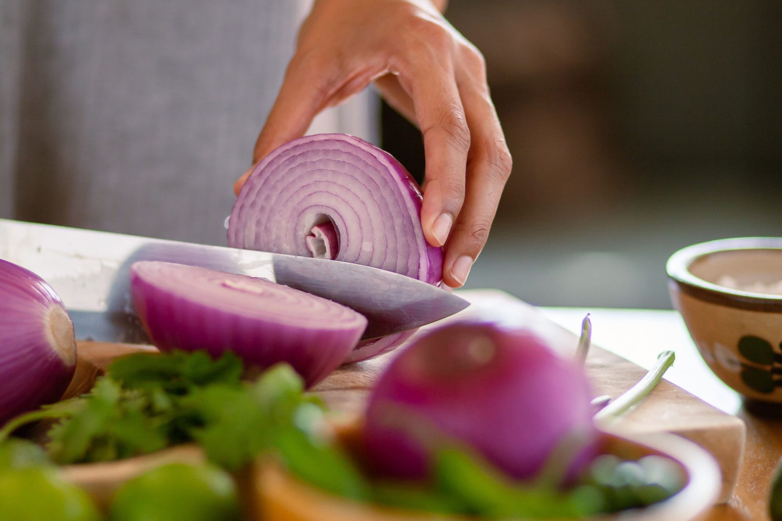 A close-up shot of a hand slicing a red onion on a wooden cutting board, showcasing freshness.